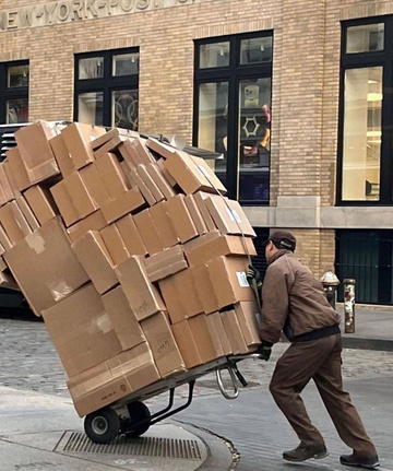 Courier wheeling a tall stack of parcels along a city street